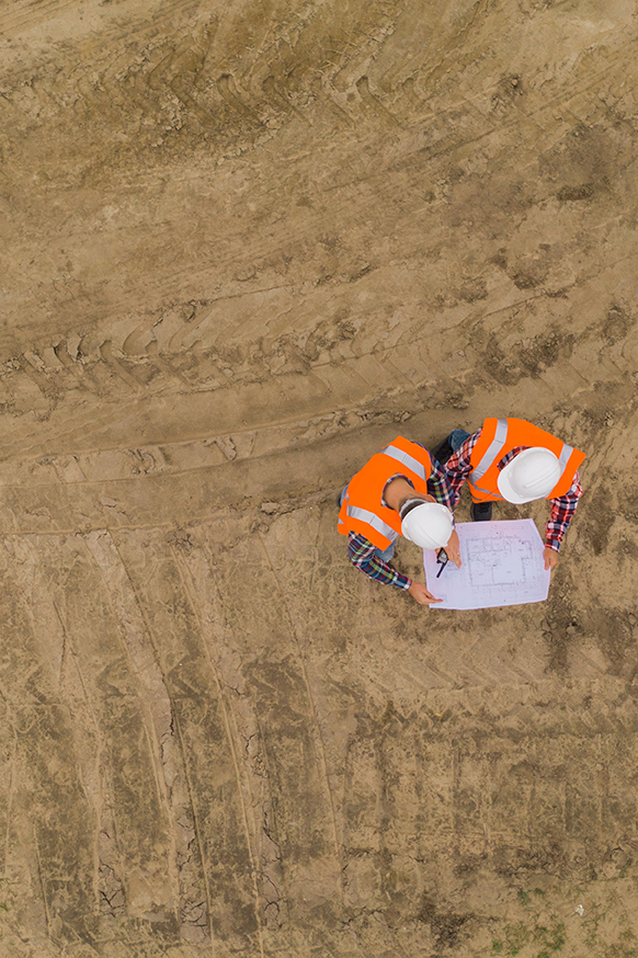 Top view of two road construction workers in orange vests and protective helmets in the middle on the field